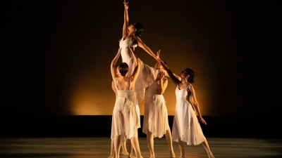 Dancers in all white holding up single dancer