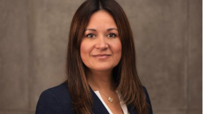 A woman with tan skin and long brown hair looks into the camera.