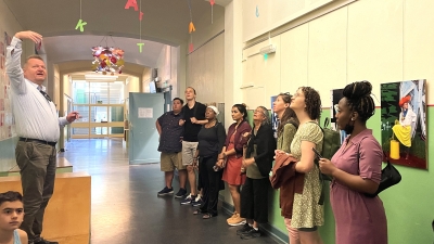A group of Astor Fellows stands in a hallway, looking up at a colorful mobile hanging from the ceiling