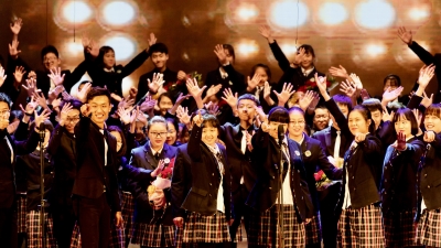 Chinese choir students in school uniforms cheering in front of spotlights