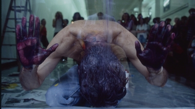 Gerald kneeling for a performance with his head on the ground and his hands painted dark purple raised above is head