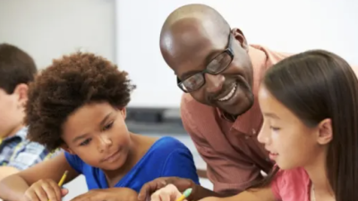 A Black teacher helping two students in classroom