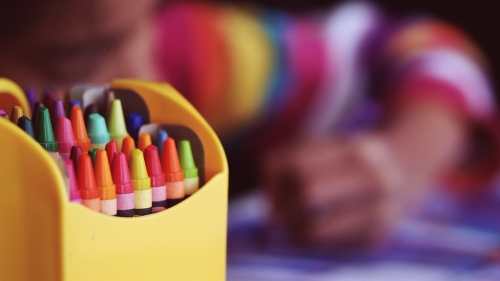 Crayons with a coloring child in the backgroun