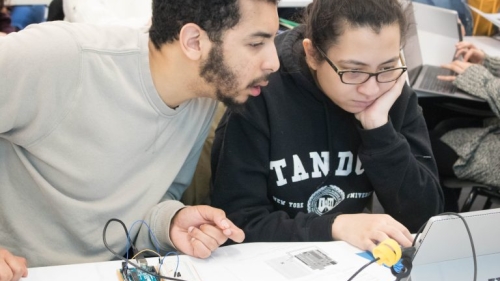 A male and female student look at a computer screen.