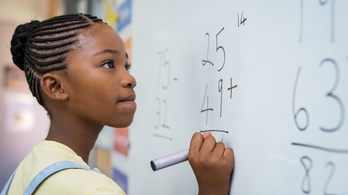 Black student solves math problems on a white board