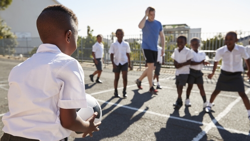 Black school children play soccer together on a sunny day