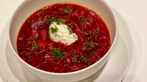 A bowl of red beet soup with dill and a dollop of white yogurt.