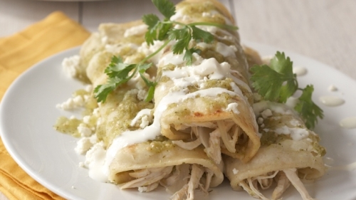 A plate of enchiladas on a plate resting on a yellow napkin.