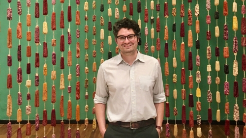 Steven McCutcheon Rubio standing in front of a curtain made of dried ears of corn hung on string.