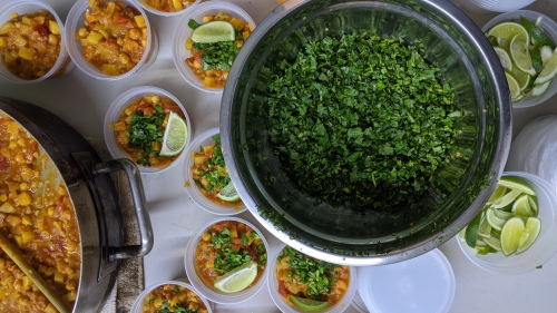 An overhead view of portions of channa masala as well as a large bowl of herbs.