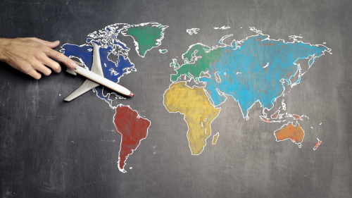 Photo of a hand guiding an airplane across a world map drawn on chalkboard