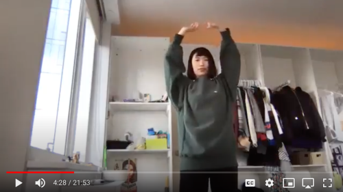 Rita Liu with her arms in the air. She stands in front of shelves filled with clothes.