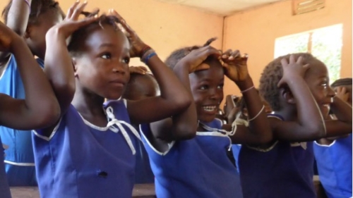 A photo of young students, all in blue school uniforms, participating in an activity where they put their hands on their heads.