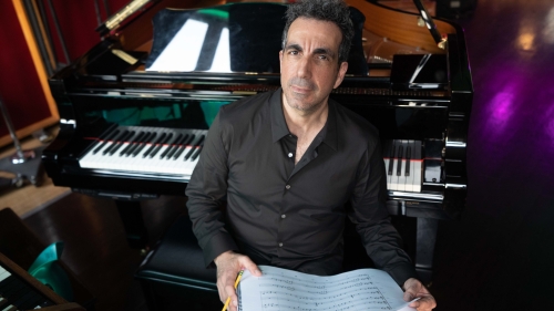 Chris Hajian sitting with his back to the piano and a musical score and pencil in his hands