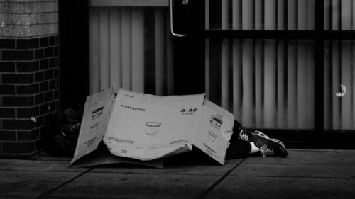 Person lying on sidewalk under a card board box