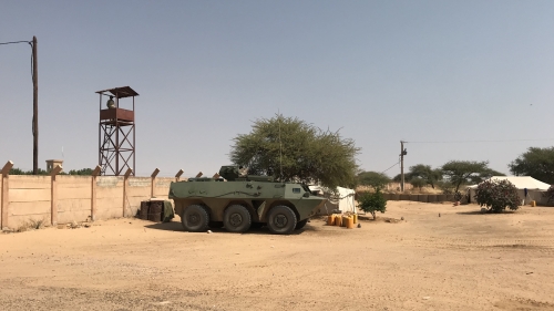 A photo of a military vehicle parked on sand in Niger next to a security tower with a watching guard