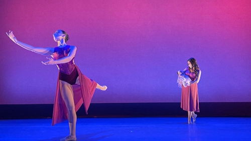 two dancers: one with her arms out and leg in the air and the other holding a baby