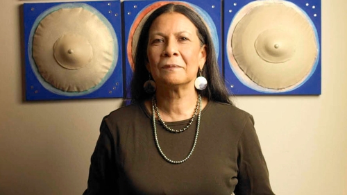 Photo of Nadema Agard in front of artwork including two, white 3D spheres on either side of her head