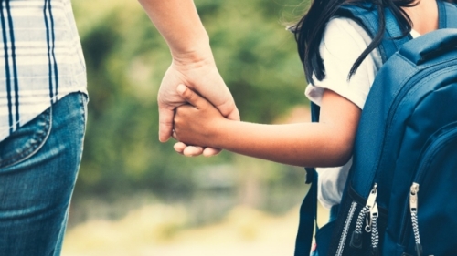A child with a backpack holds a parent's hand.  
