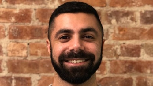 Waahid standing in front of a brick wall wearing a white cardigan sweater