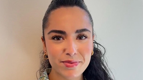 Arantxazu in front of a white wall looks at the camera with her hair pulled back in a pony tail.