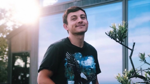 Travis sits on a deck outside with his hands in his pockets.