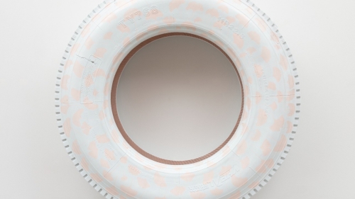 A tire, painted in very light pink and blue speckles, against a white backdrop. 