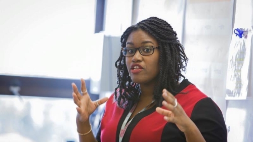 Erika Hardaway, a Black women in a red and black dress, speaks at the front of a classroom. 