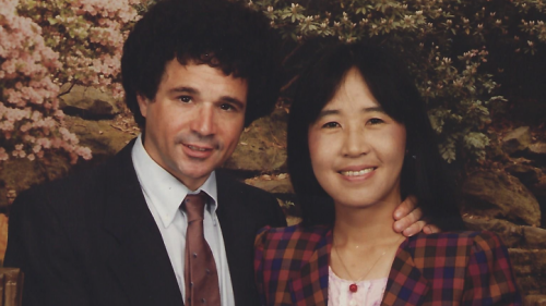 Okhee Lee and her husband, Michael B. Salwen, hold hands and smile at the camera.