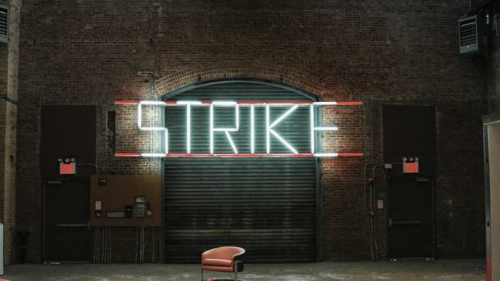 Wall mounted, white fluorescent tubes that spell STRIKE
