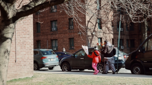Parent and child are walking with wrapped flowers into an affordable housing residential area.
