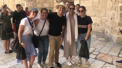 Five smiling students stand by an ancient stone wall in Israel
