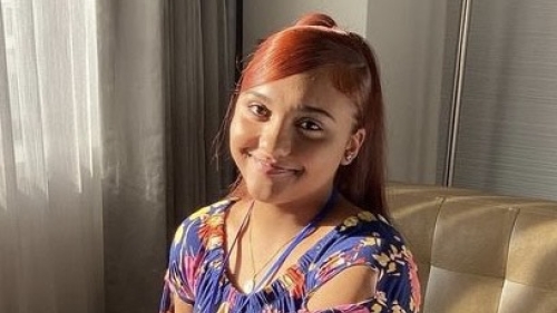 High School student with red hair sits on a tan couch smiling at the camera. 