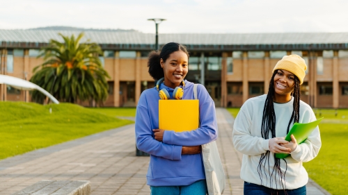 Two Black teenage girls walking down an outdoor walkway with their school books.