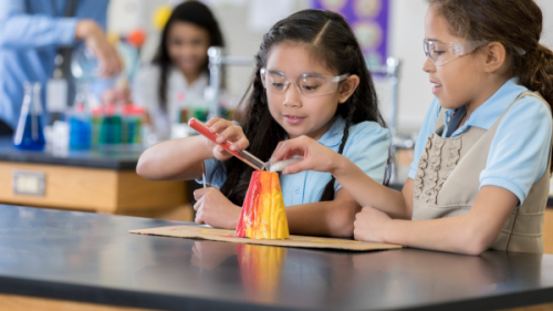 Two girls in science class performing an experiment on a volcano model
