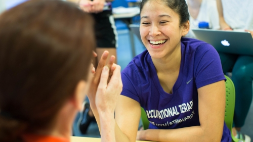 Two occupational therapy students smile as they do an OT exercise. 