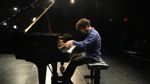 Piano student playing grand piano with spotlights on him