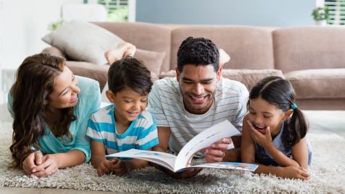 Image captures a mother and father reading with their two children, one boy, and one girl.