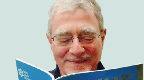 Image captures head shot of NYU Metro Center's Norm Fruchter reading an issue of VUE. Norm wears eye glasses and smiles as he reads the journal.