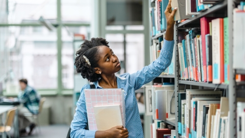 Student grabbing a book from a shelf in a library.