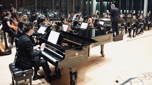 Full orchestra performing with piano in forefront