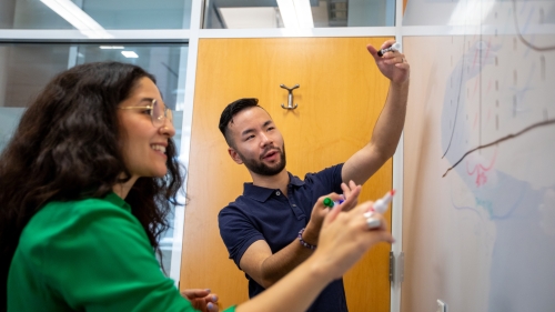 2 students conversing about their work and writing on a dry erase board