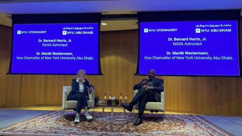 A photo of Mariet Westermann and Bernard Harris, Jr. seated on stage, participating in a discussion in front of two slides that say "Bernard Harris, Jr., NASA Astronaut / Mariet Westermann, Vice Chancellor New York University Abu Dhabi"