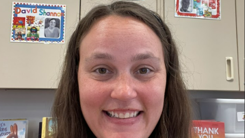 Headshot of Sudha Narsipur. Photo features teacher sitting in her classrrom, smiling as she takes the photo in front of her classroom cobinents.