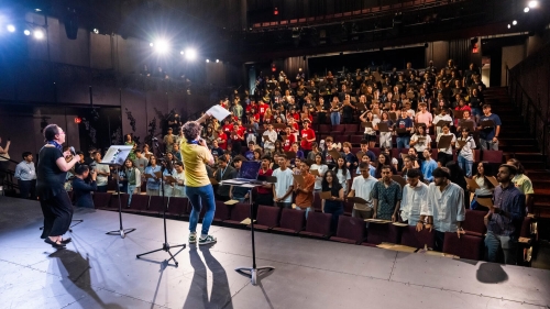 A crowd of students looks at the stage, where 2 people lead an activity