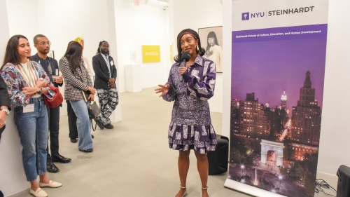 Cuppy speaks in front of a sign that says NYU Steinhardt