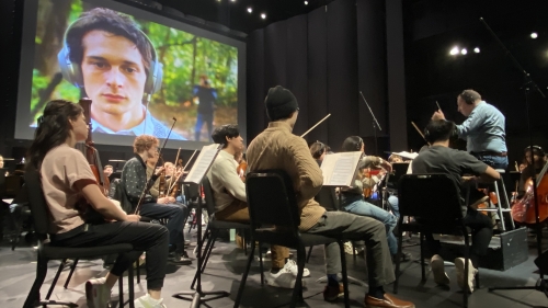Students playing instruments in front of screen created by screen scoring students