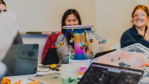 A carousel with LEGO figures spins in the foreground as two students smile in the background