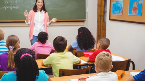 Female teacher in front of blackboard teaching math problems to middle school children sitting at desks