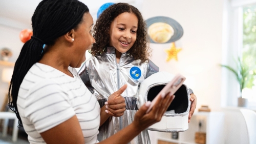 Black mother plays with her young daughter dressed as an astronaut and holding her helmet